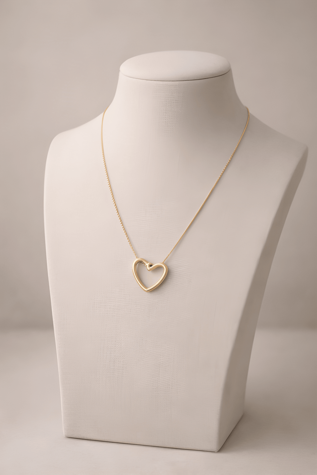 Gold heart pendant necklace displayed on ivory bust stand