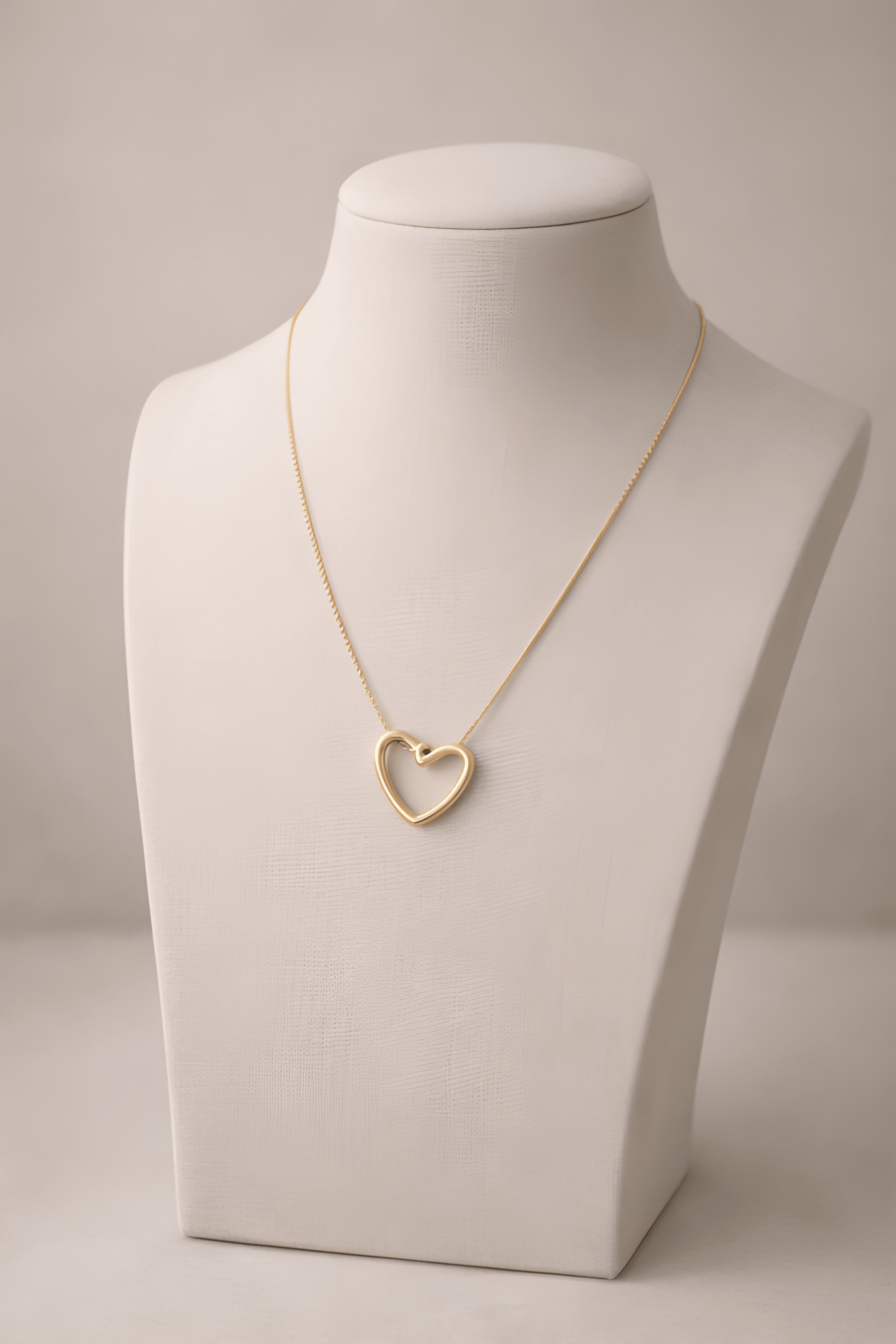 Gold heart pendant necklace displayed on ivory bust stand