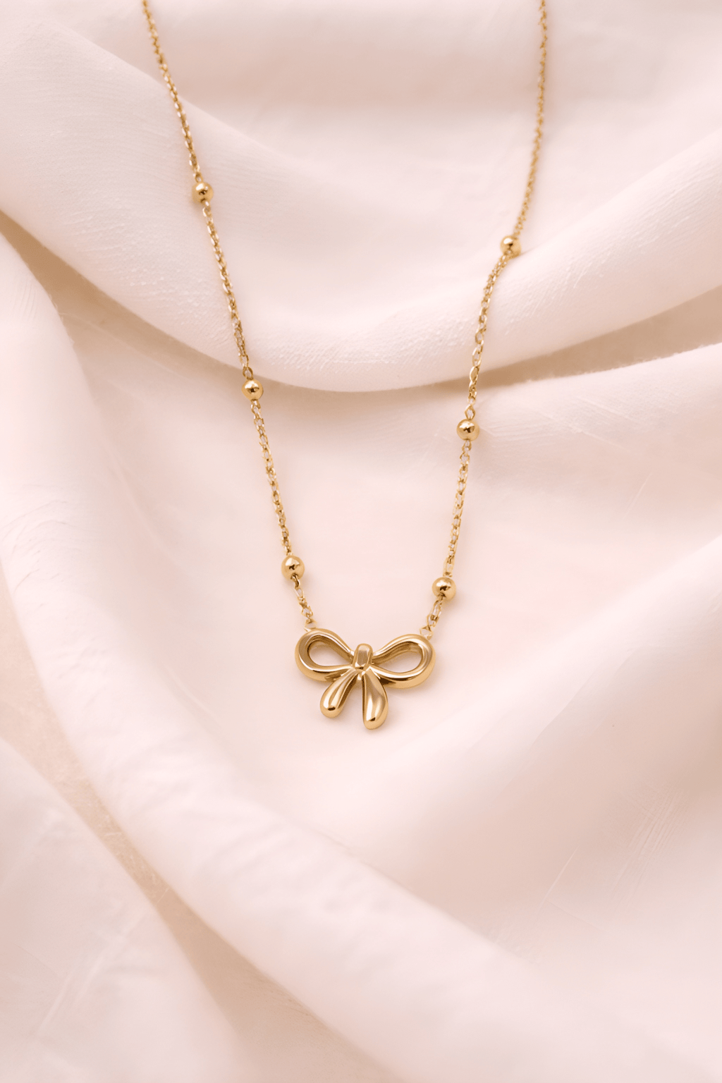 Minimal gold bow pendant necklace on soft neutral background