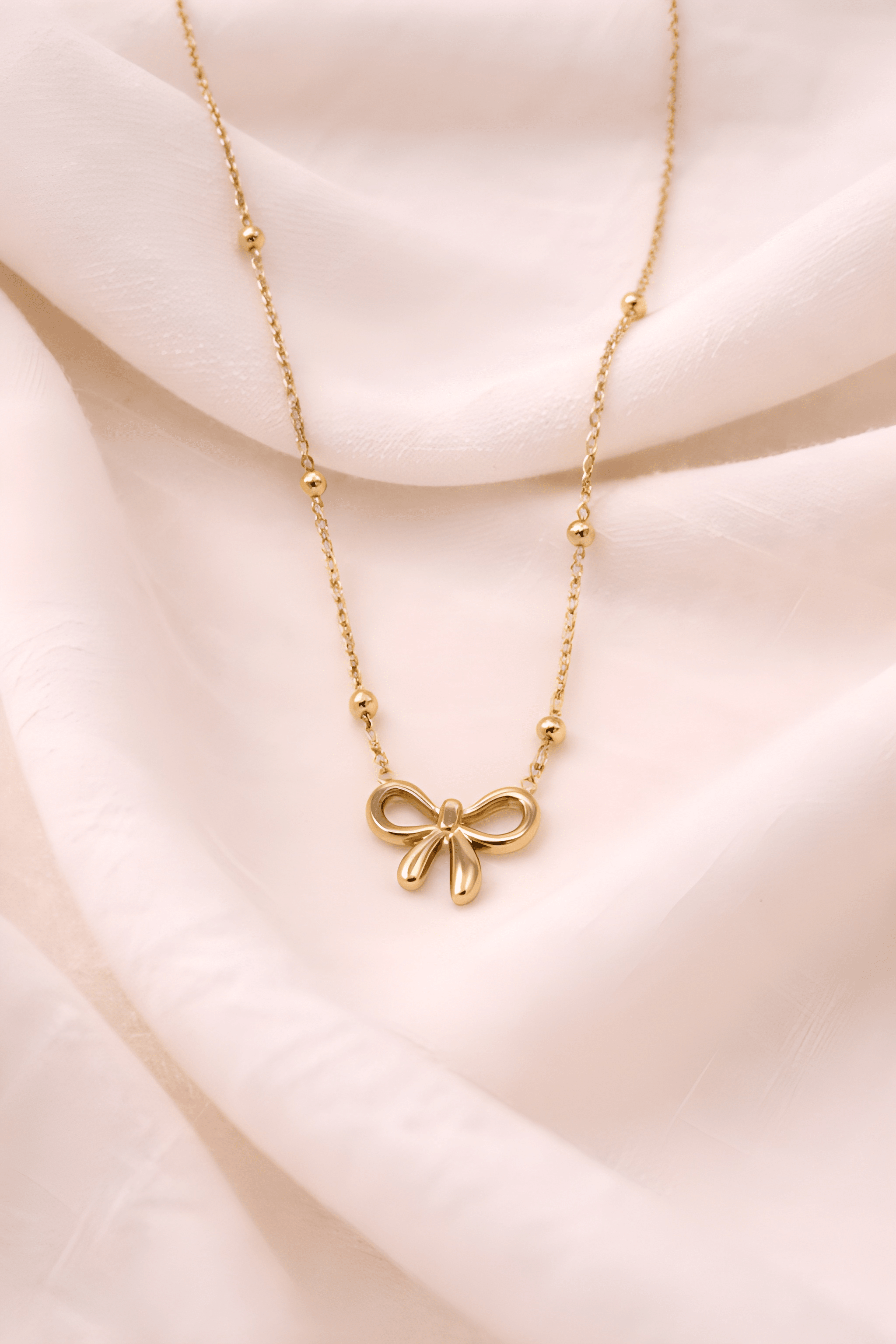 Minimal gold bow pendant necklace on soft neutral background