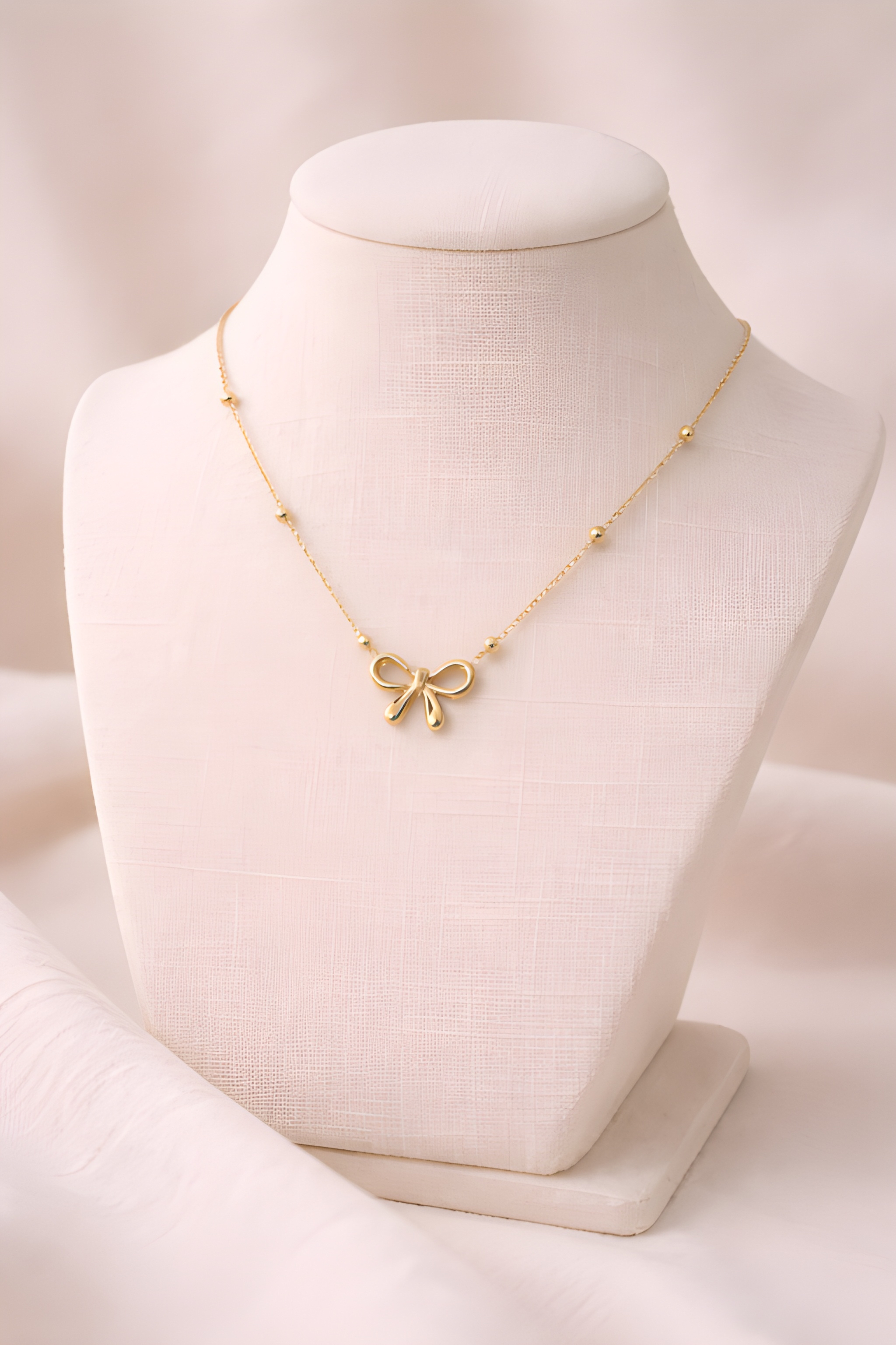 Gold bow pendant necklace displayed on ivory bust stand