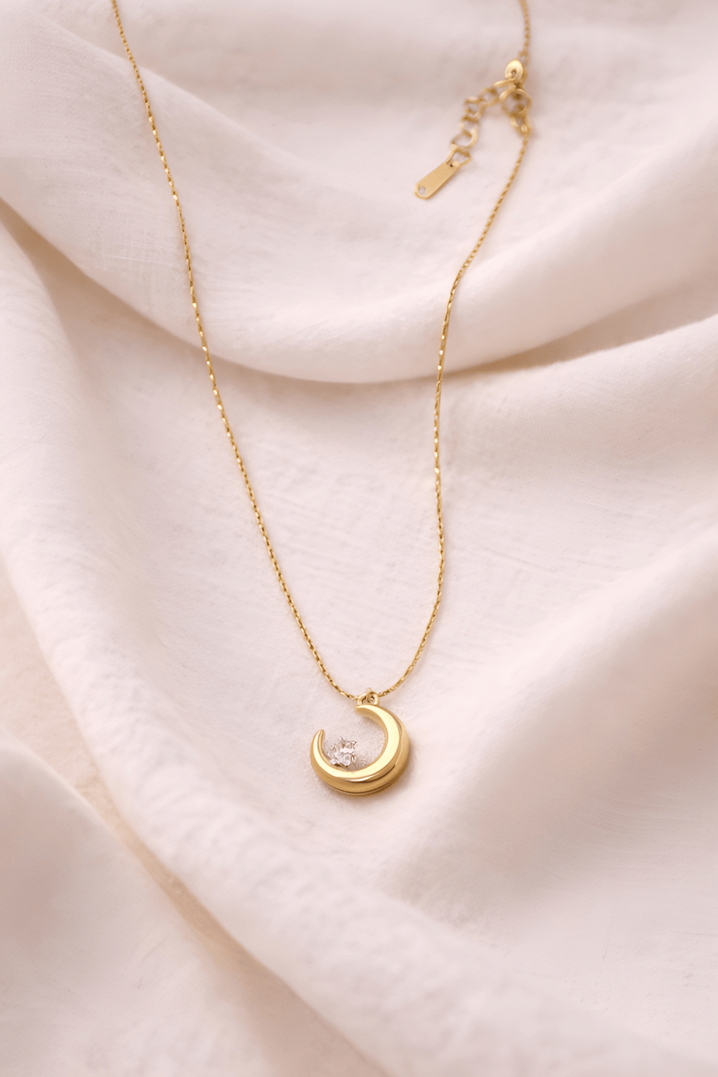 Gold crescent moon pendant necklace with crystal on neutral background