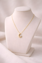 Gold crescent moon pendant necklace displayed on ivory stand