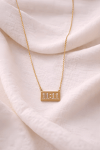 Gold 11:11 rectangular bar pendant necklace on neutral background