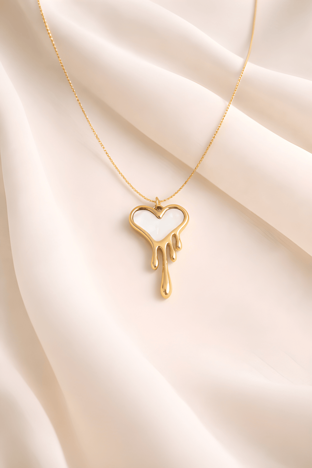 Gold dripping heart pendant necklace with white enamel on neutral background