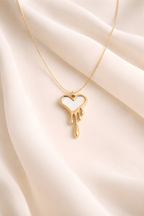 Gold dripping heart pendant necklace with white enamel on neutral background