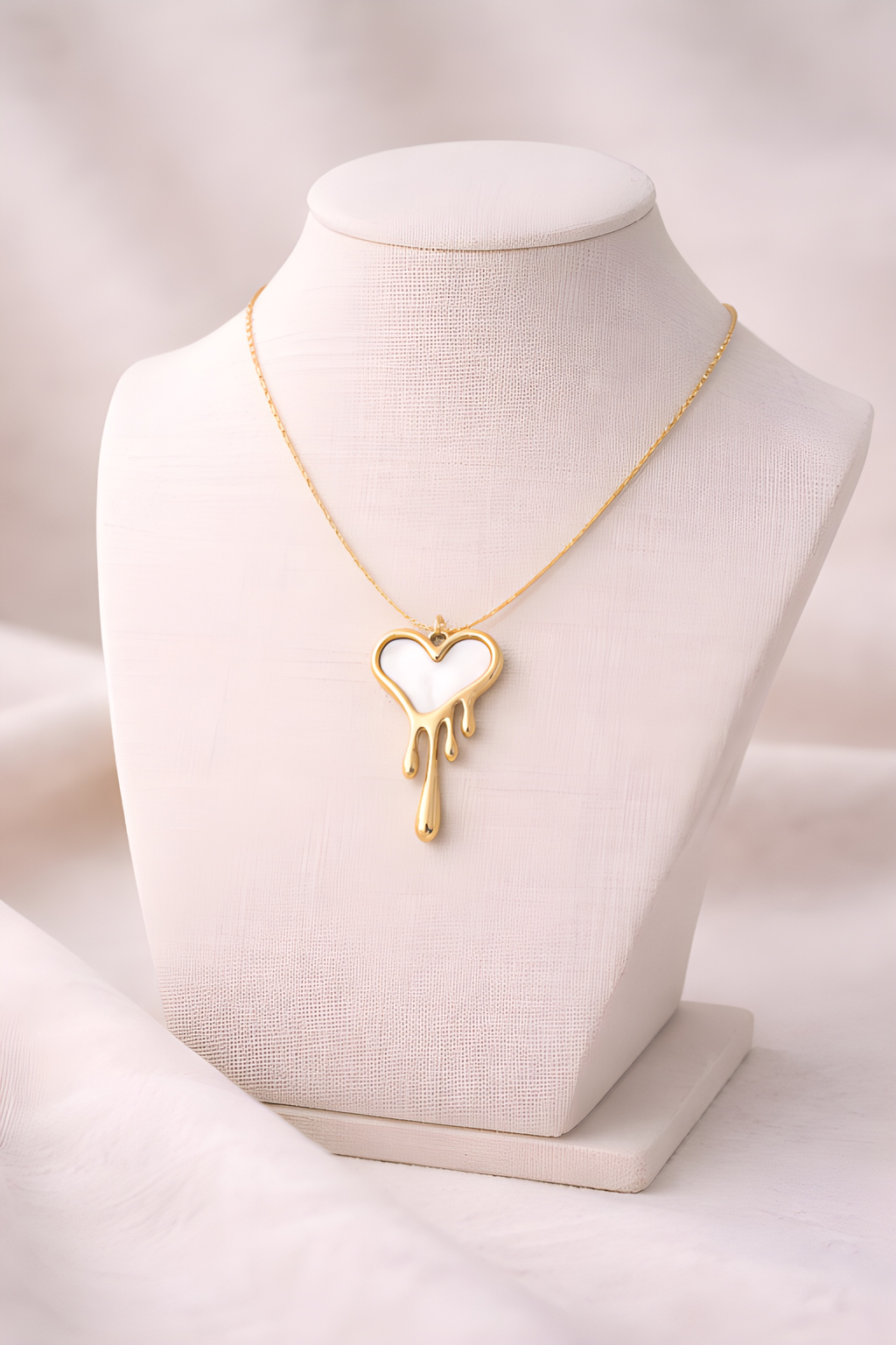 Dripping heart gold pendant necklace displayed on ivory bust stand