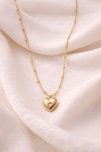 Gold heart pendant necklace with center stone on neutral background