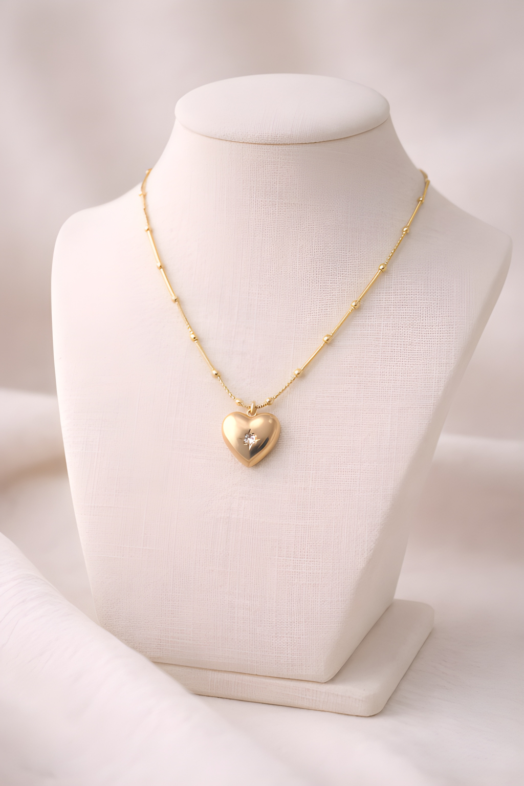 Gold heart pendant necklace with structured bead bar chain on ivory stand