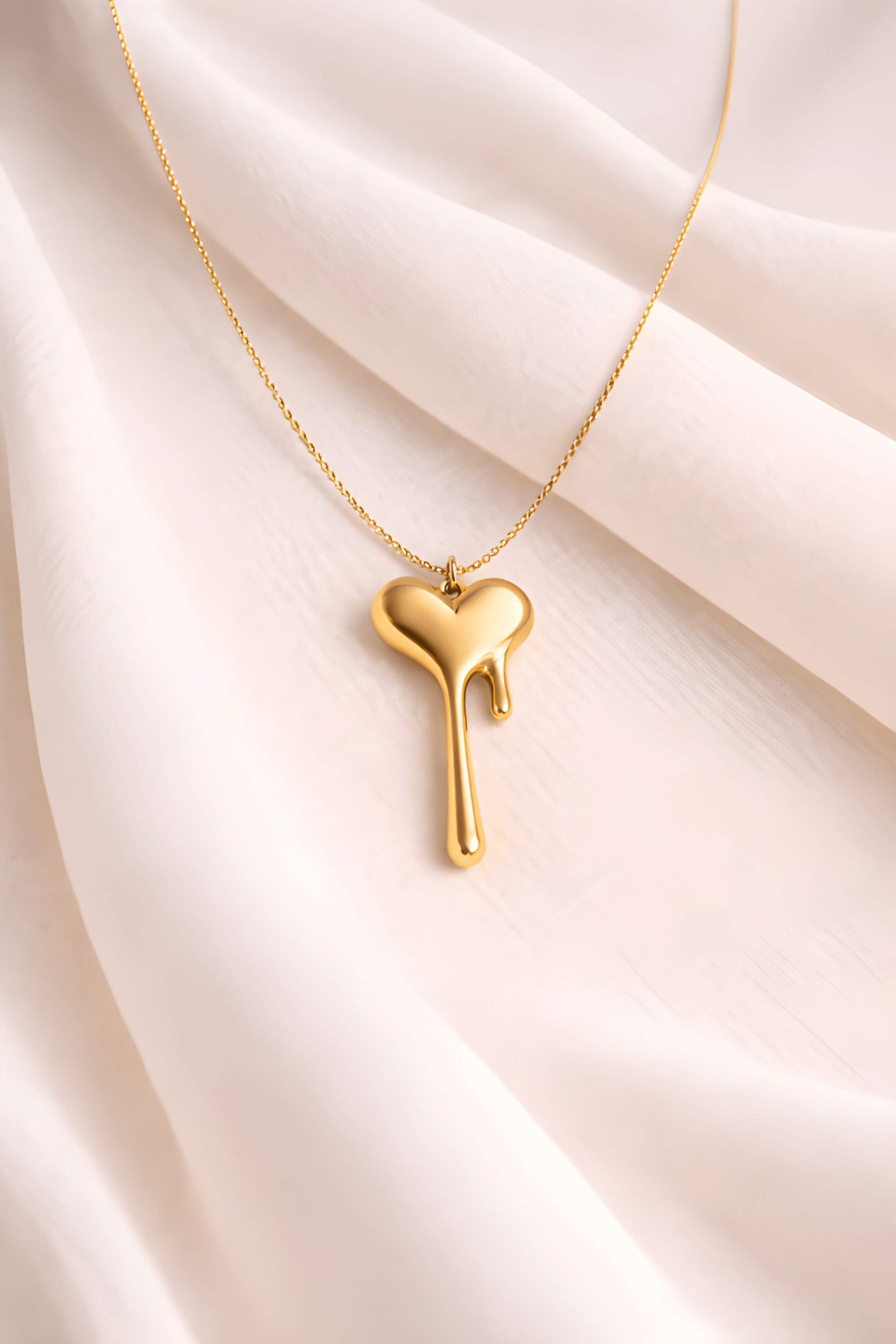 Gold melting heart pendant necklace on soft ivory fabric