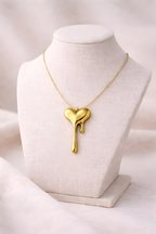 Gold melting heart pendant necklace displayed on ivory stand