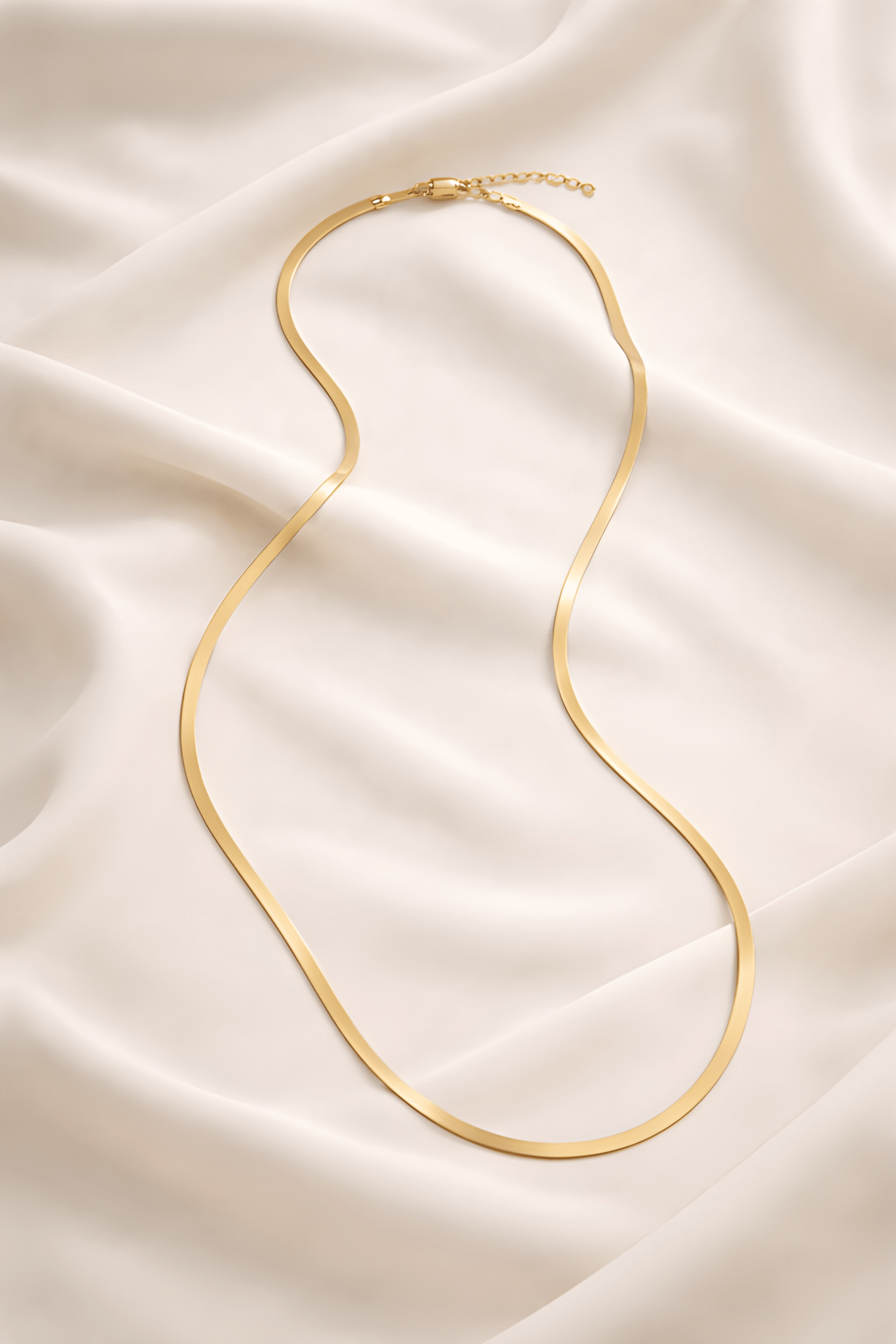Minimal gold snake chain necklace on ivory fabric background