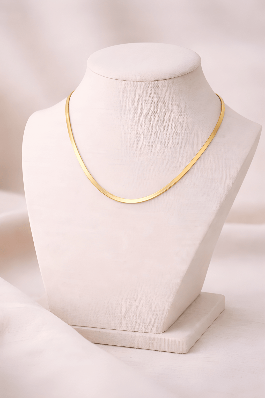 Gold flat snake chain necklace displayed on ivory bust stand