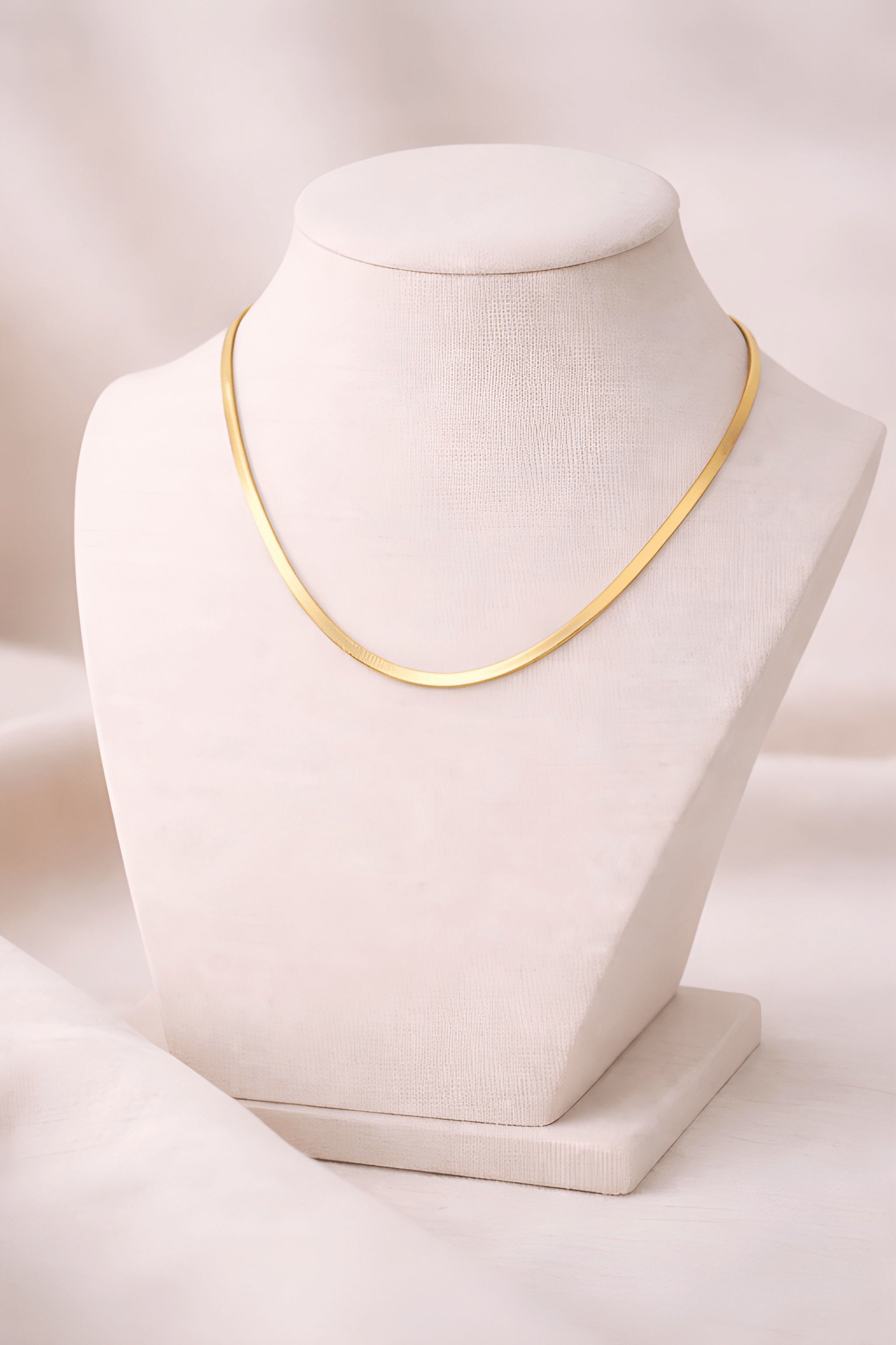 Gold flat snake chain necklace displayed on ivory bust stand