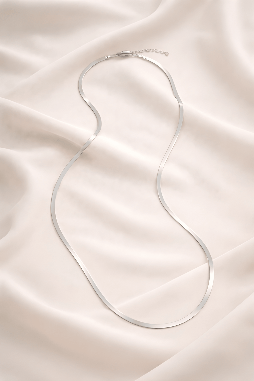 Minimal silver snake chain necklace on ivory fabric background