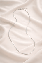 Minimal silver snake chain necklace on ivory fabric background