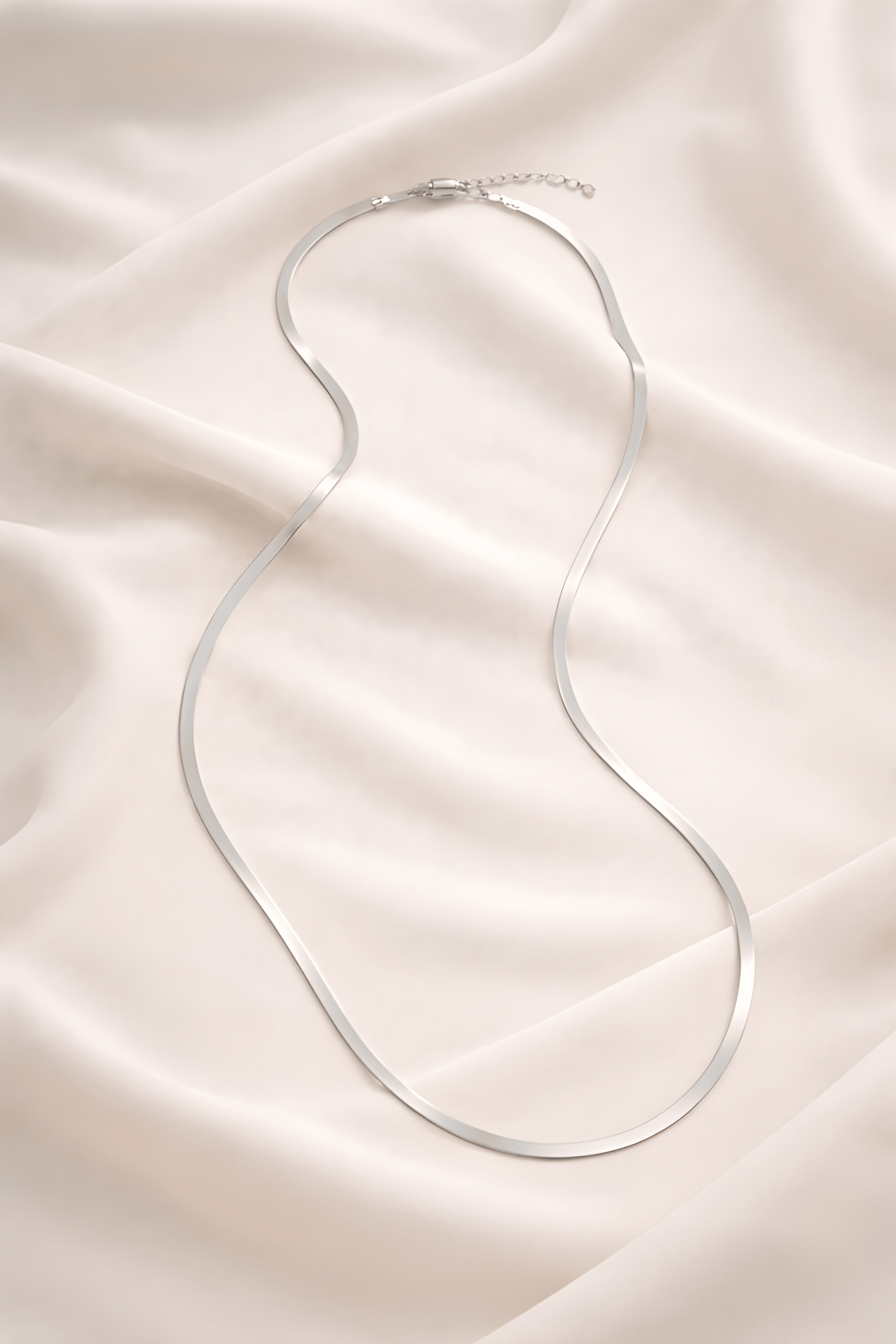 Minimal silver snake chain necklace on ivory fabric background