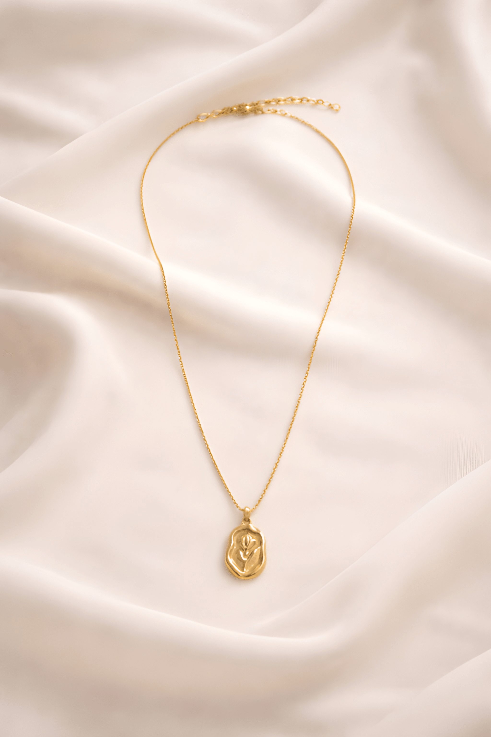 Minimal gold rose pendant necklace on ivory fabric background
