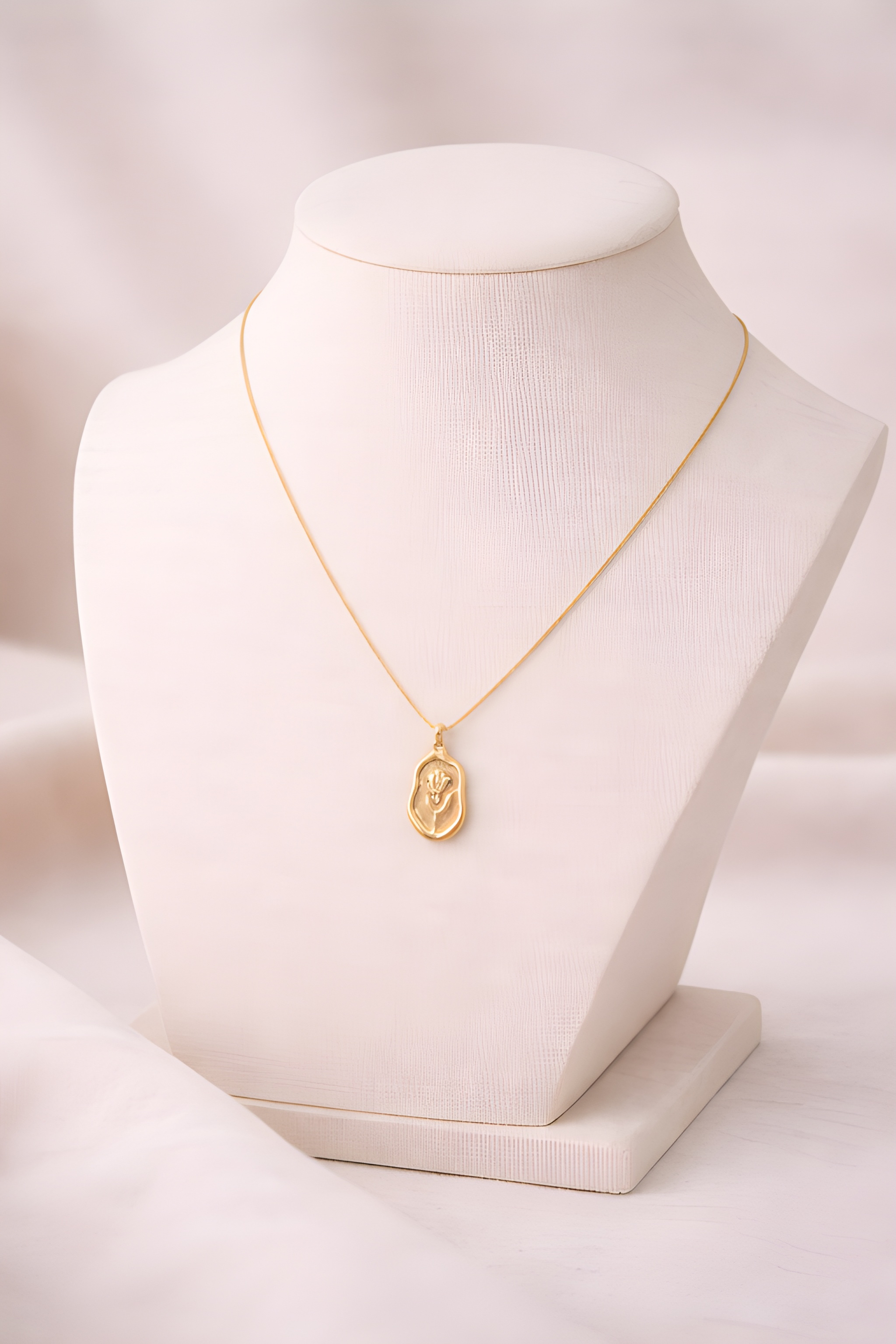 Gold rose engraved pendant necklace displayed on ivory bust stand