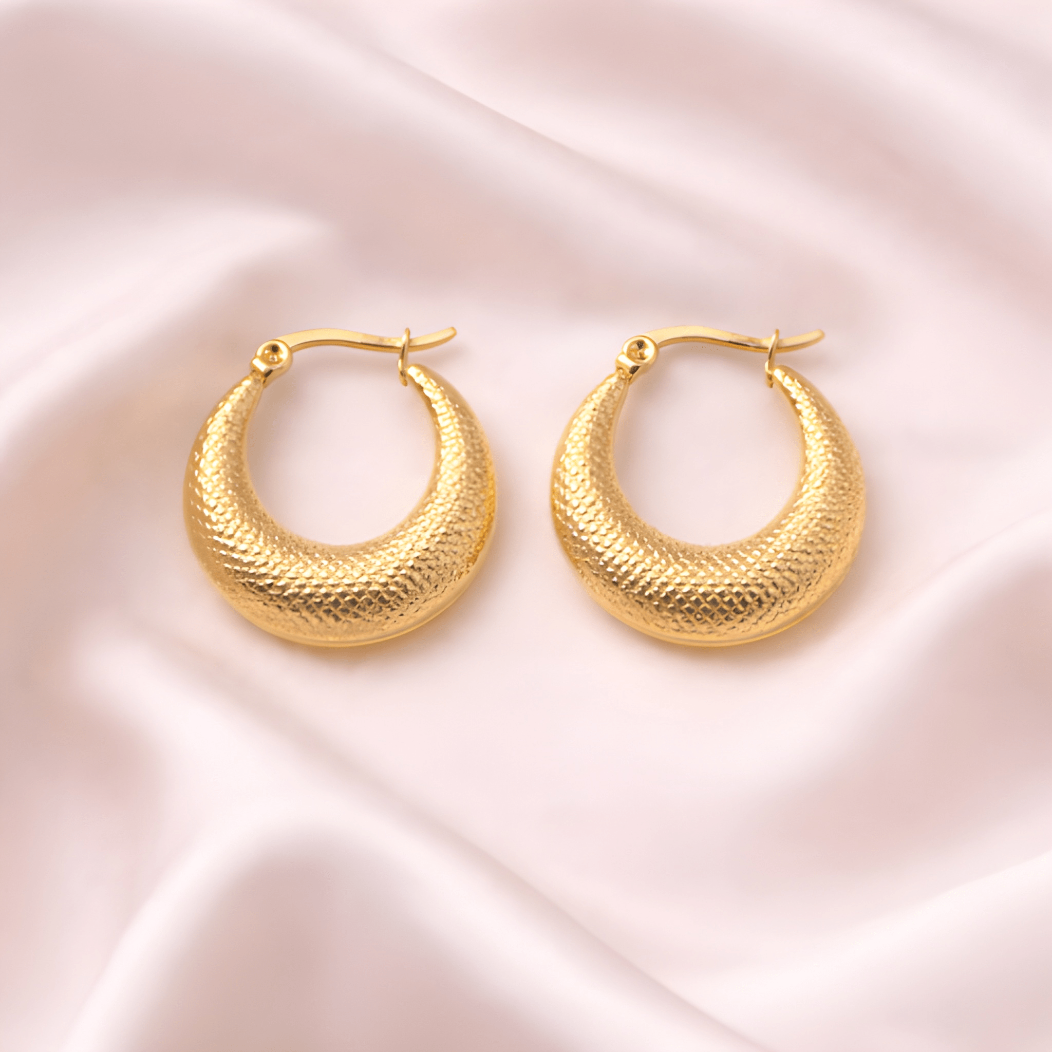 Textured gold crescent hoop earrings on soft blush satin fabric