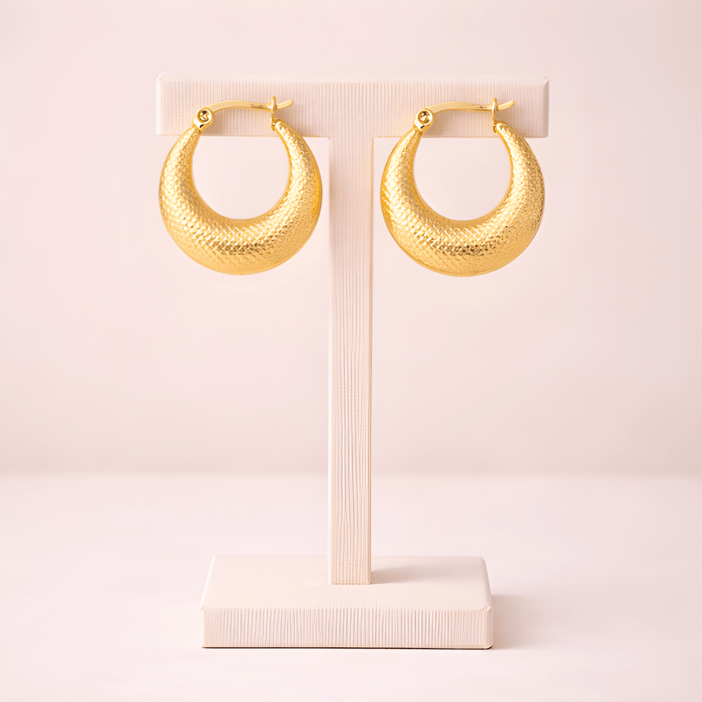Textured gold crescent hoop earrings displayed on ivory stand