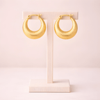 Textured gold crescent hoop earrings displayed on ivory stand