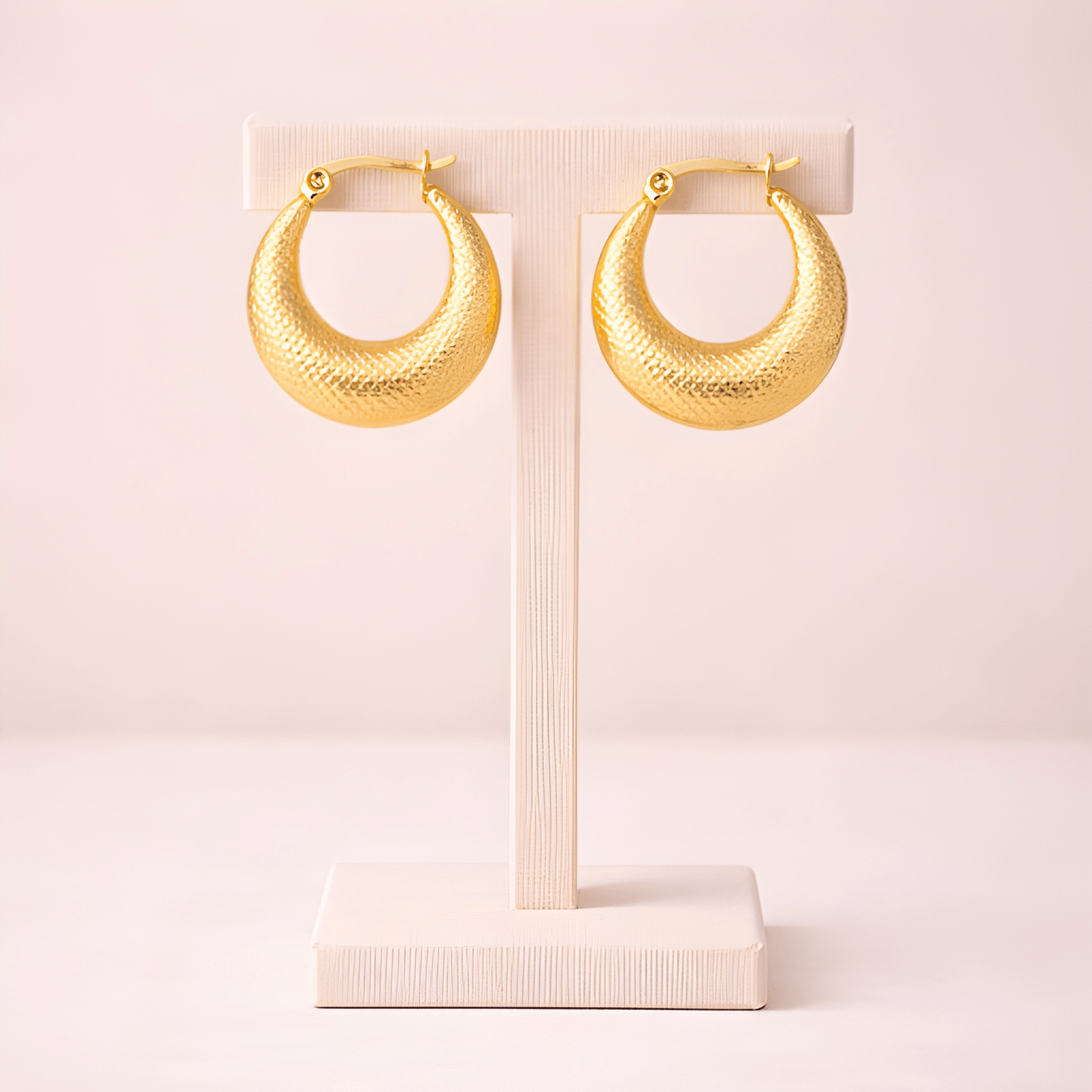 Textured gold crescent hoop earrings displayed on ivory stand