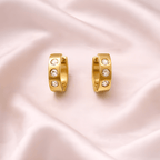 Crystal studded gold huggie hoop earrings on soft blush satin background