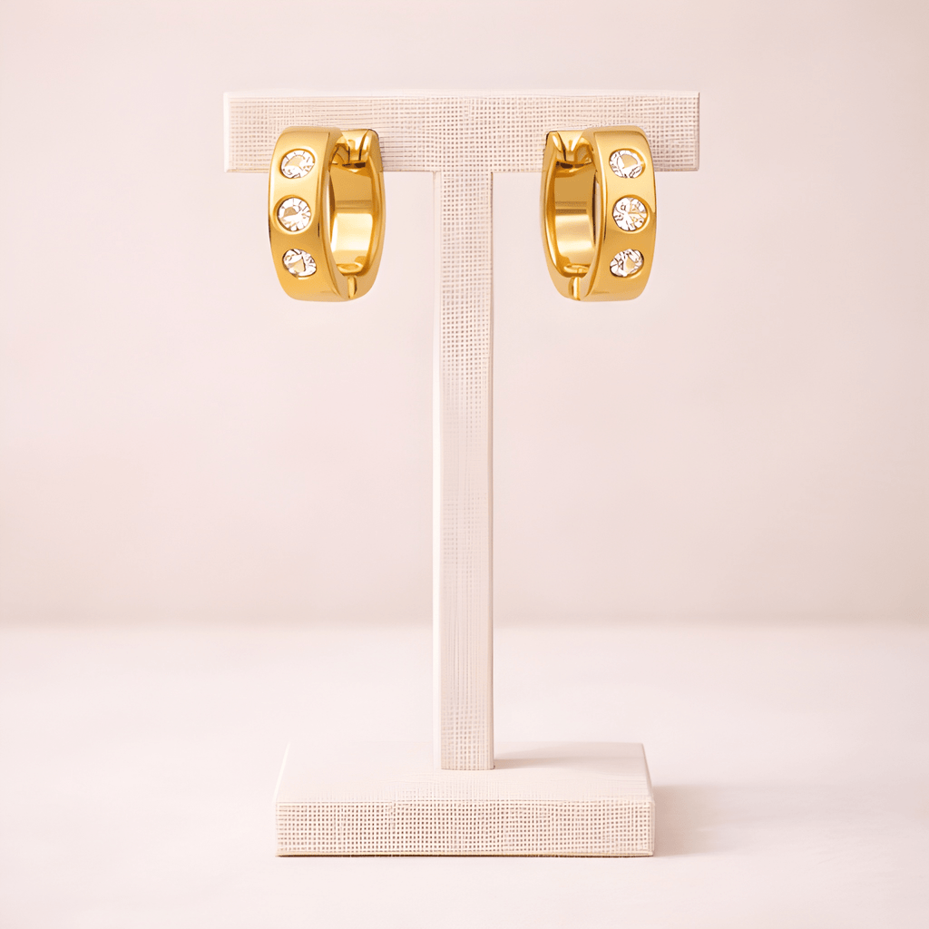 Crystal studded gold huggie hoop earrings displayed on ivory stand