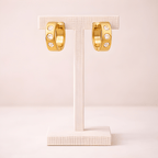 Crystal studded gold huggie hoop earrings displayed on ivory stand