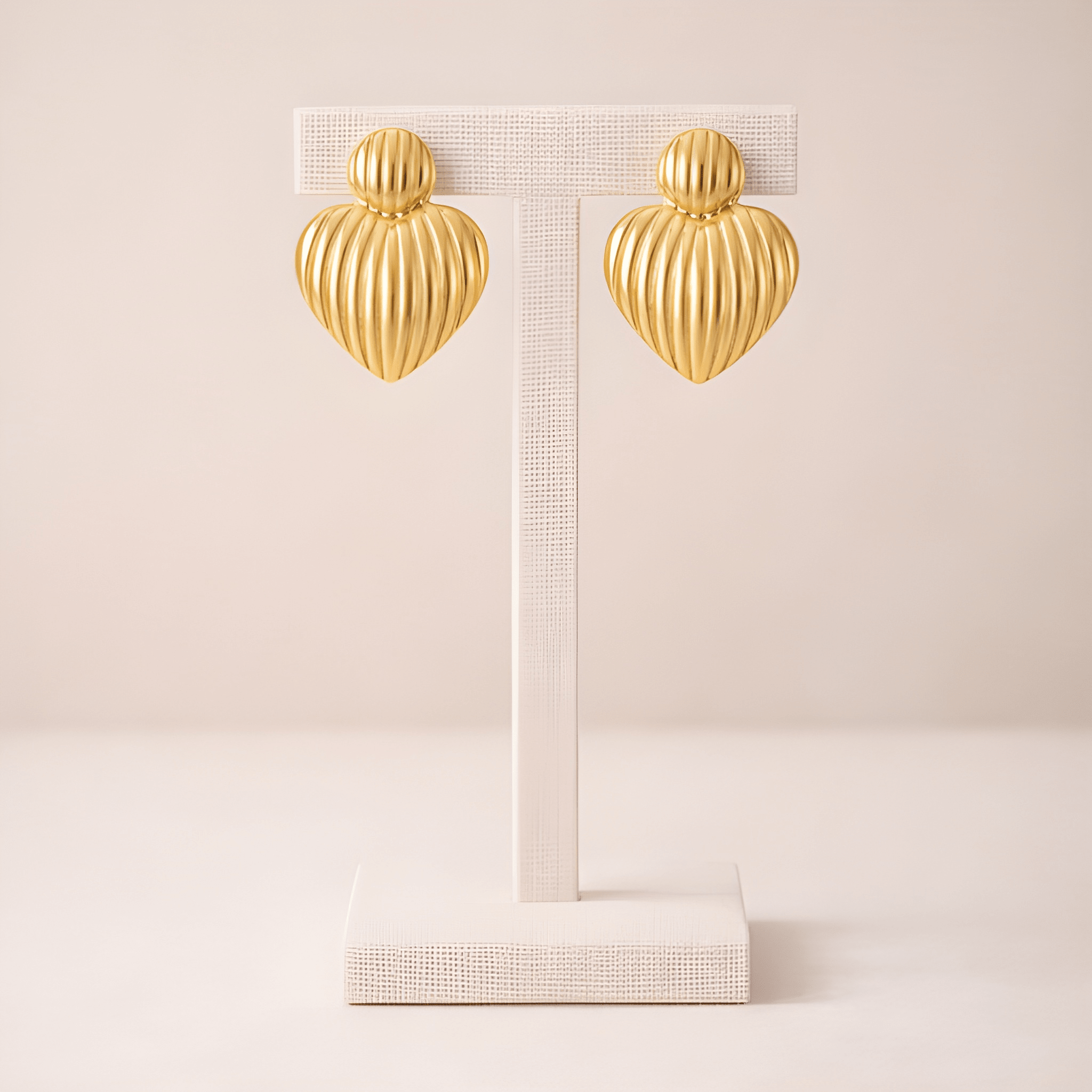 Ribbed gold heart stud earrings on ivory stand