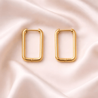 Rectangular gold hoop earrings on soft neutral fabric