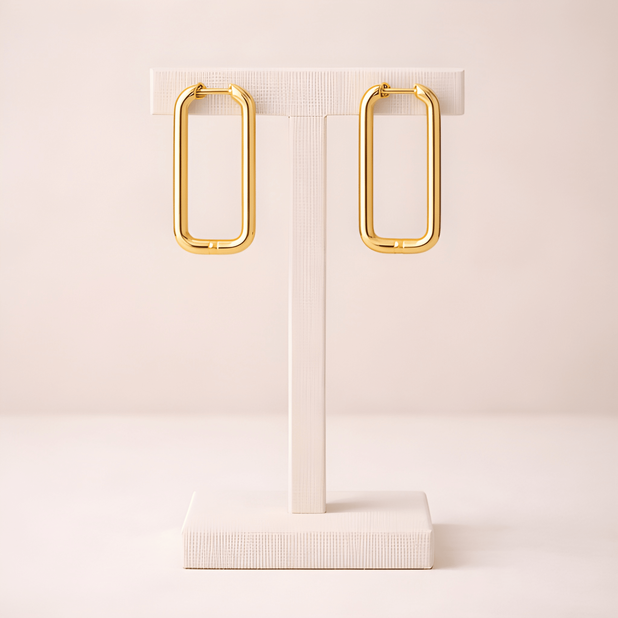 Rectangular gold hoop earrings on ivory stand