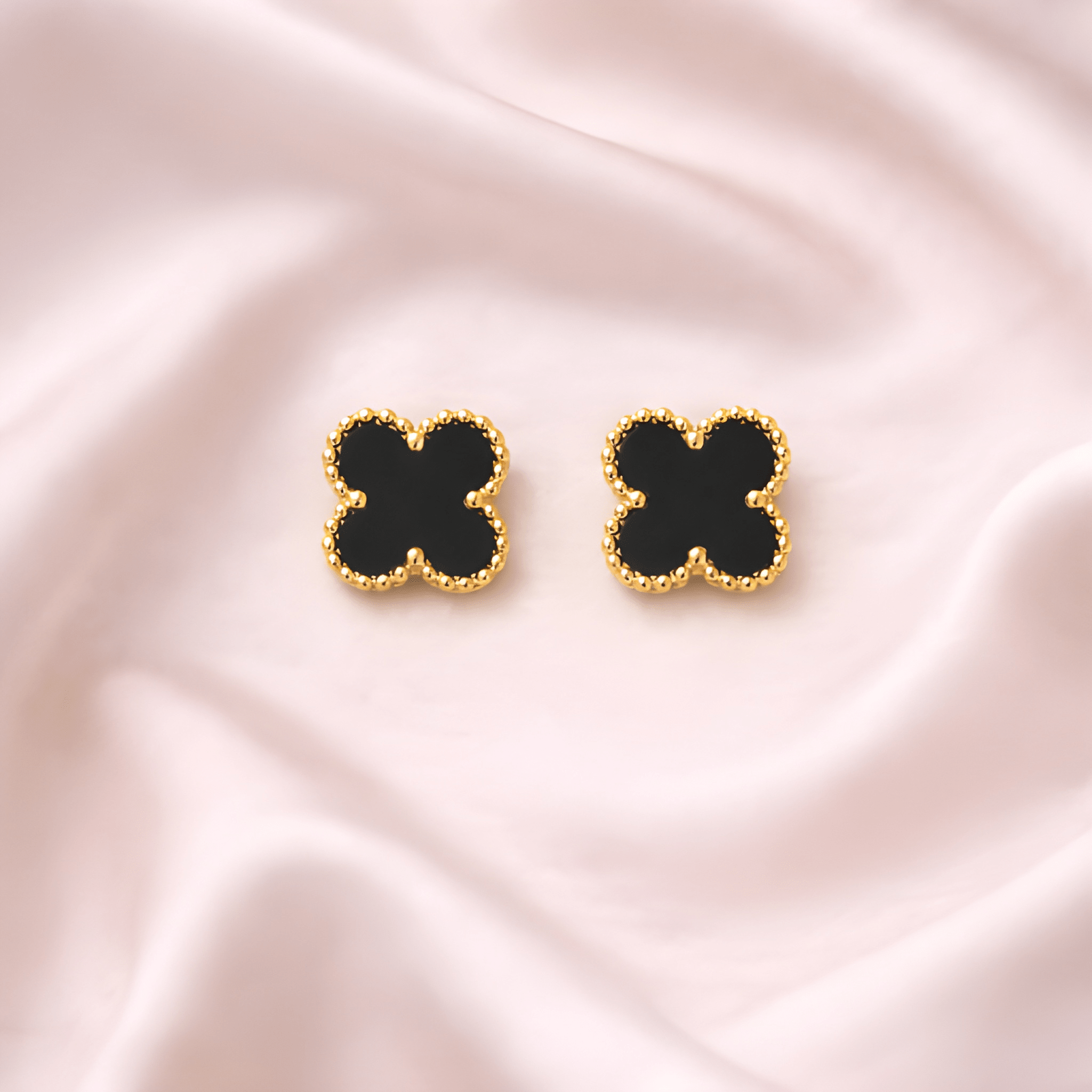 Black clover stud earrings with gold beaded frame on soft ivory background