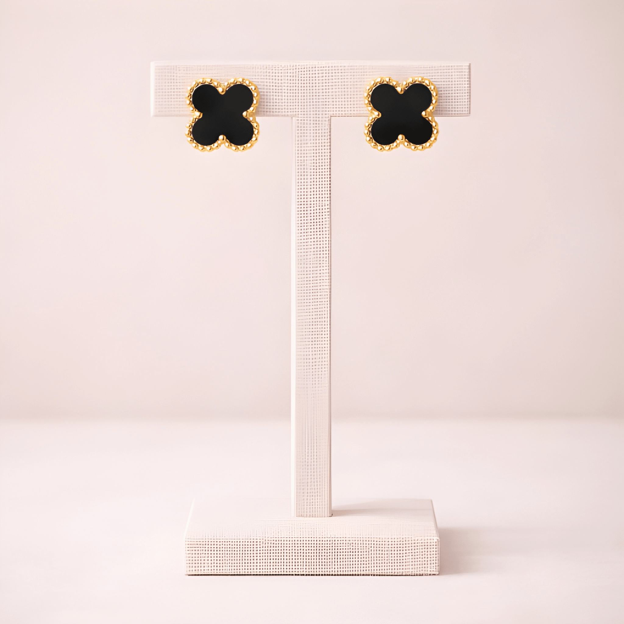 Black clover stud earrings displayed on ivory stand