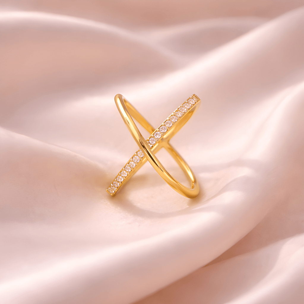Minimal X crystal gold crossover ring on blush satin fabric