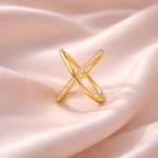Minimal X crystal gold crossover ring on blush satin fabric
