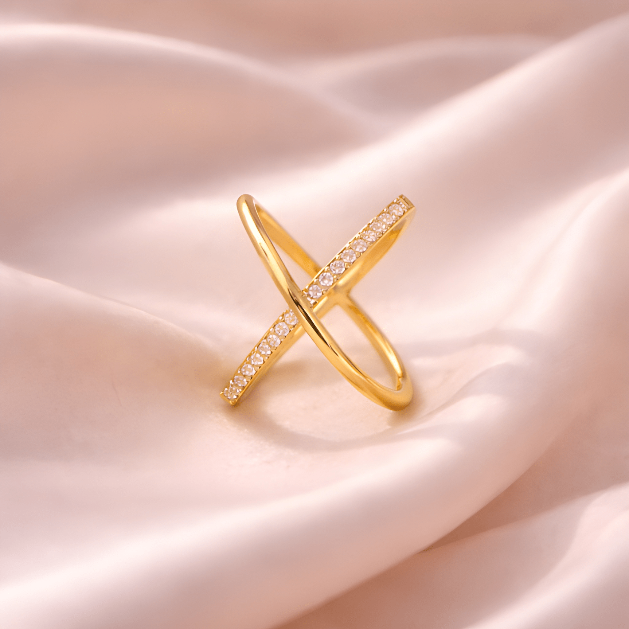Minimal X crystal gold crossover ring on blush satin fabric
