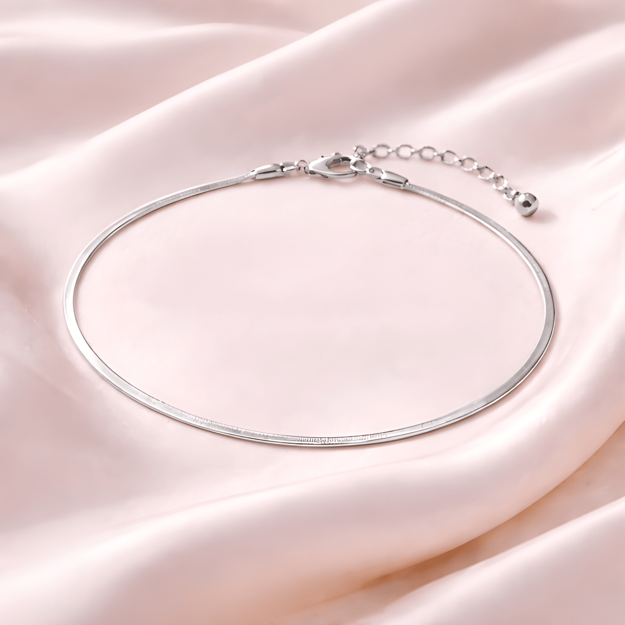 Minimal silver snake chain anklet on blush satin fabric