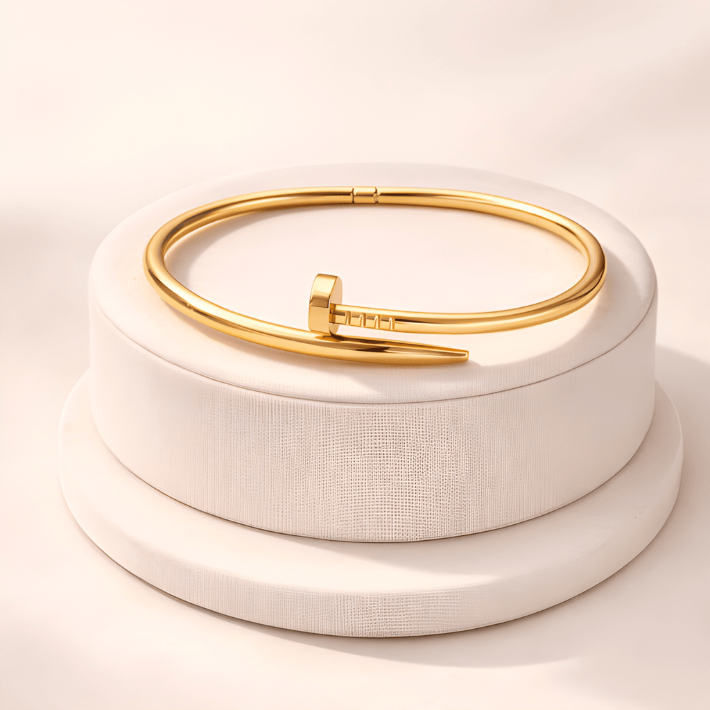 Gold nail-inspired bangle bracelet displayed on ivory podium