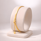 Gold snake chain bracelet with dangling heart charm displayed on ivory stand