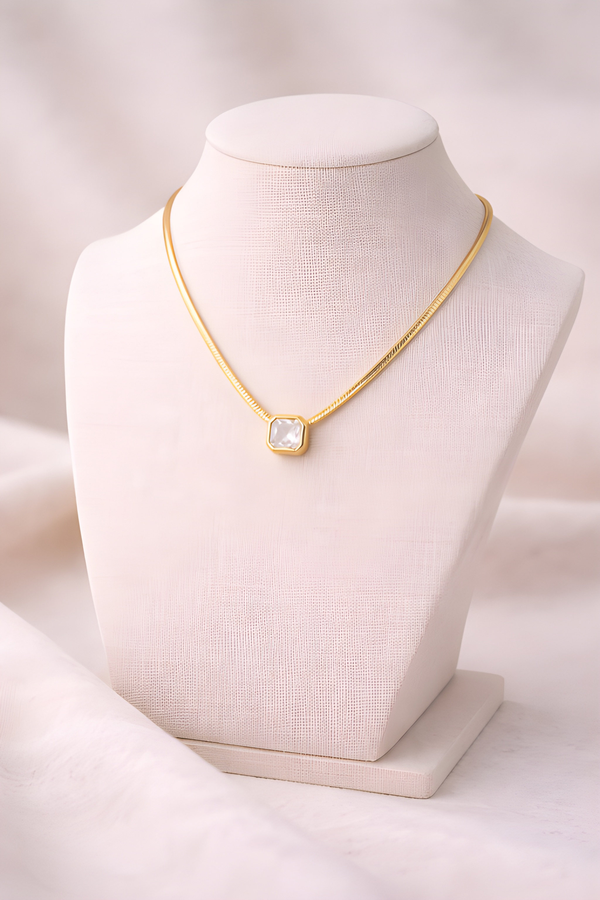 Gold snake chain necklace with white rectangular pendant on ivory stand