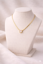 Gold snake chain necklace with blush pink rectangular pendant on ivory stand