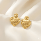 Minimal gold ribbed heart stud earrings on soft fabric