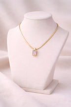 Gold snake chain necklace with blush pink rectangular crystal pendant on ivory stand